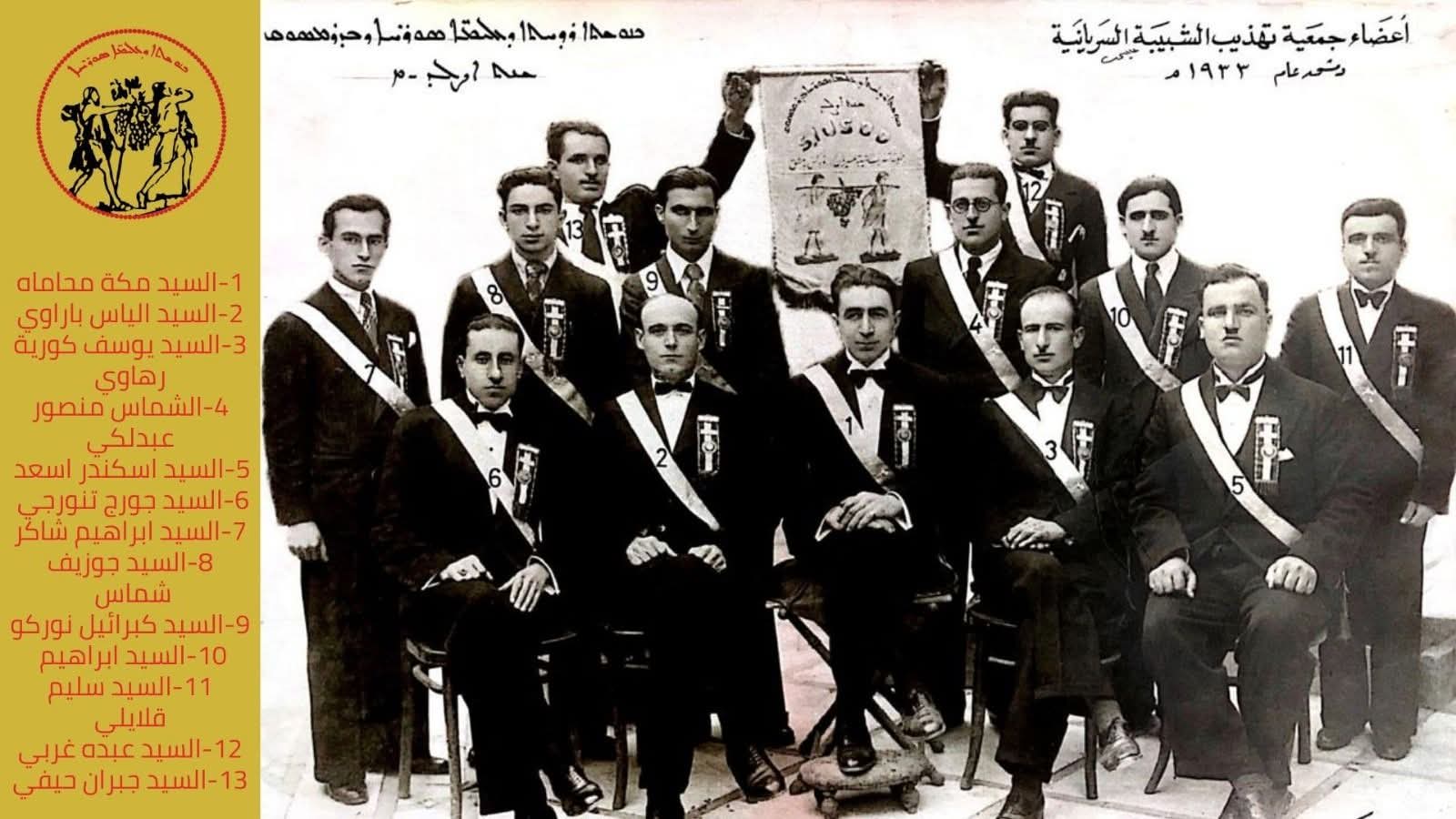 Black and white 1933 group portrait of thirteen association members wearing sashes, beside the association banner